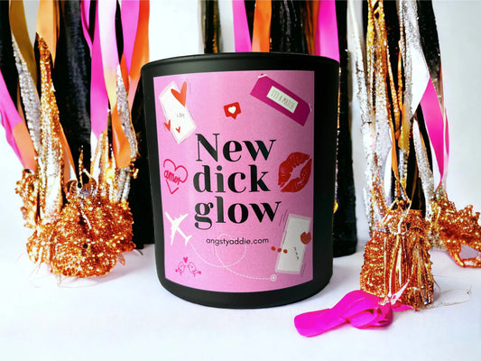 Black "New dick glow" candle with pink label, surrounded by pink and gold tinsel fringe decor