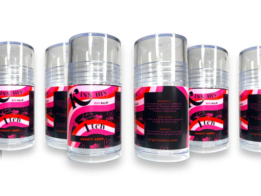 Row of "Kiss My Itch" bug balm stick containers with pink and black labels showing ingredients
