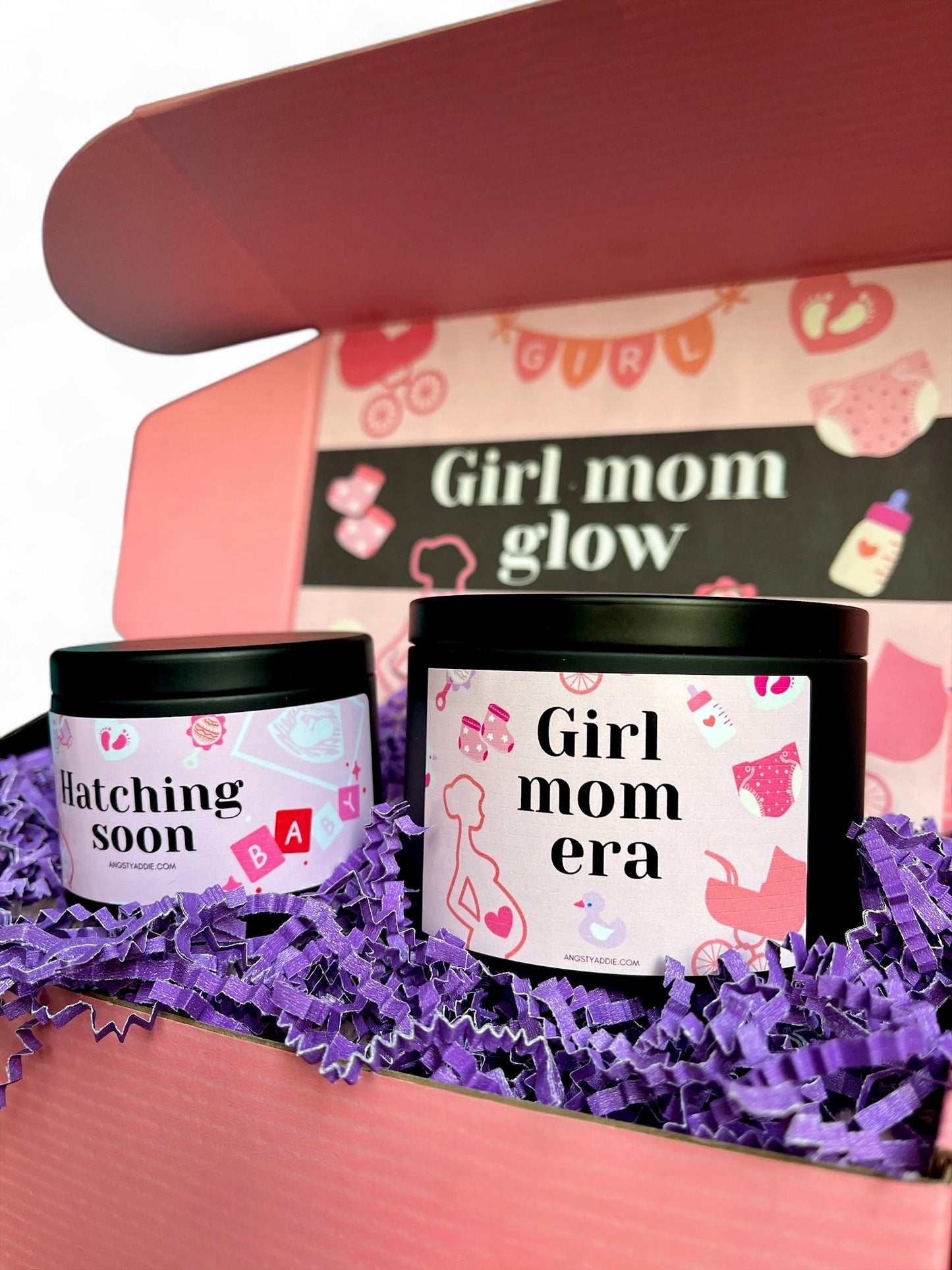 A pink box containing two candles labeled "Hatching soon" and "Girl mom era" is shown, with a pink and white design featuring baby-related icons.