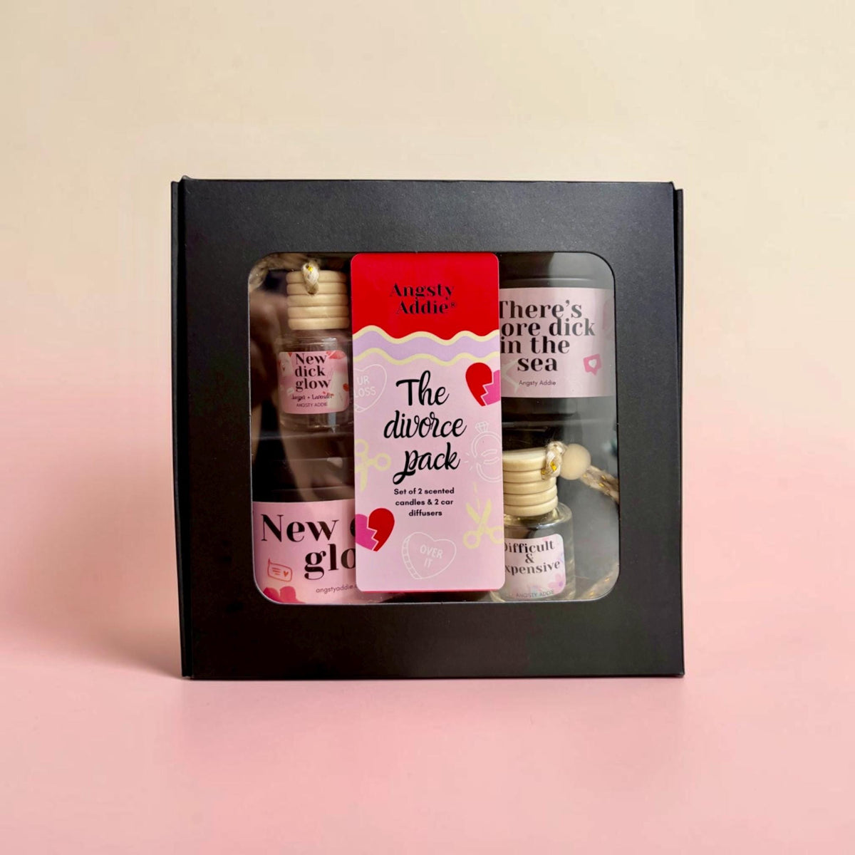 a set of four small bottles, each with a unique label, arranged in a black box against a pink background.