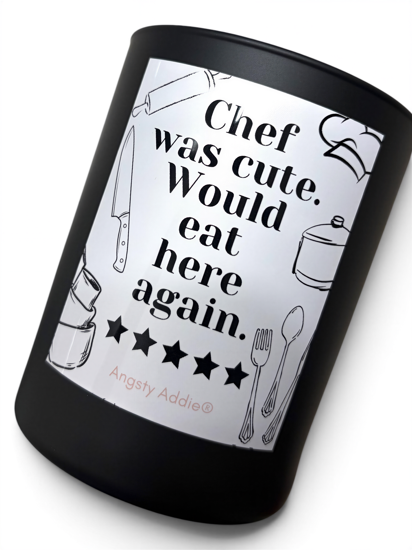 a black candle holder with a white label that reads "Chef was cute. Would eat here again." The candle holder has a black rim and is placed on a white surface.