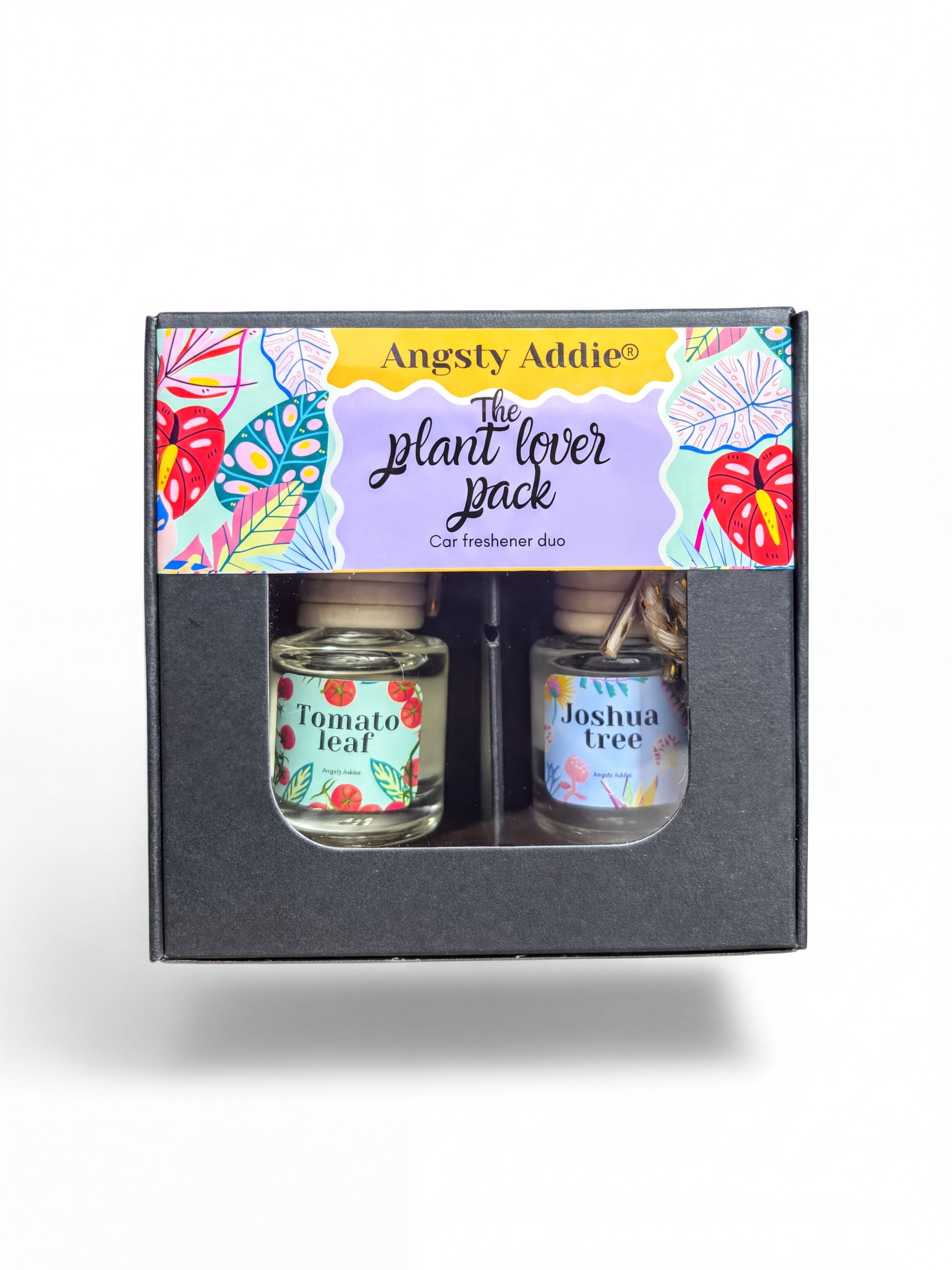 a set of two small glass bottles with labels, placed inside a black box with a colorful, tropical-themed design.